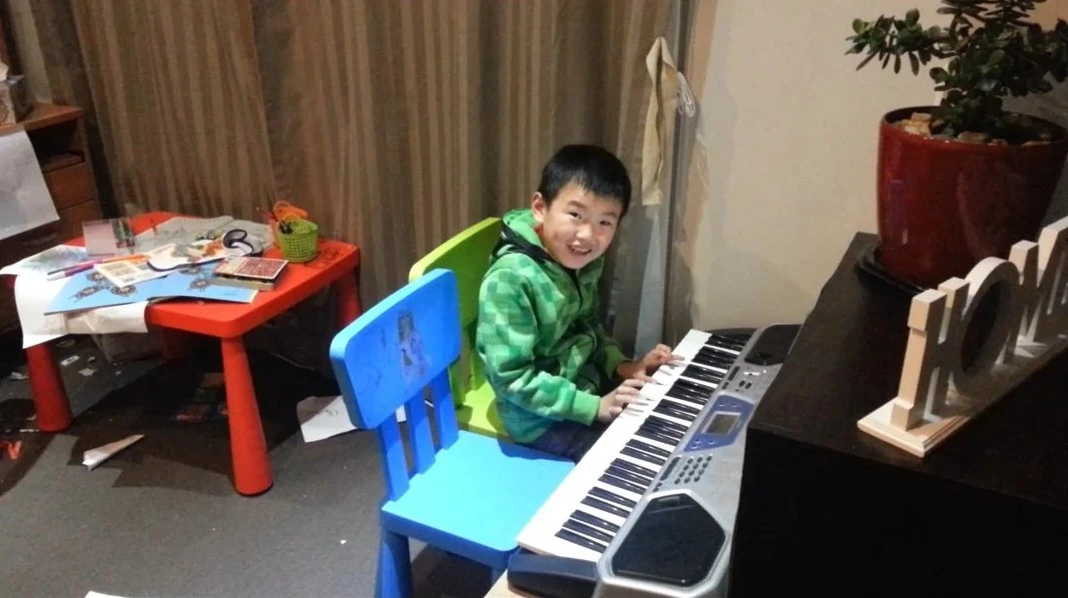 Young Isaac in a green jacket discovering music on a small Casio keyboard