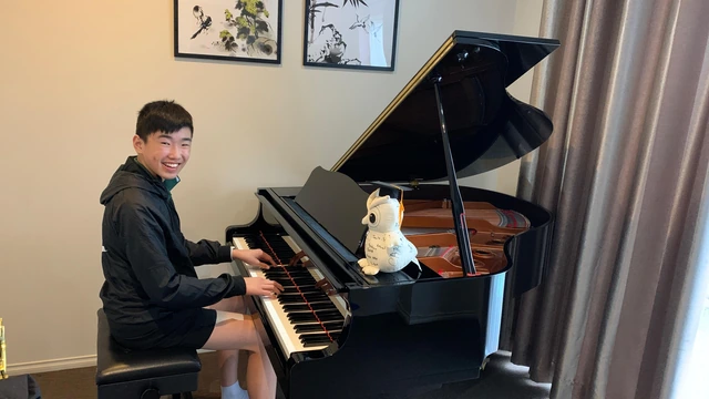 Isaac smiling at his Yamaha grand piano