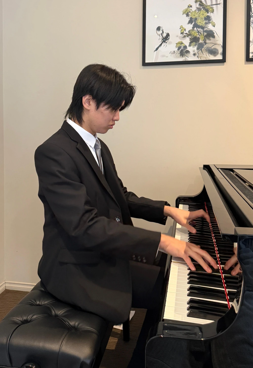 Isaac playing the grand piano in a black suit